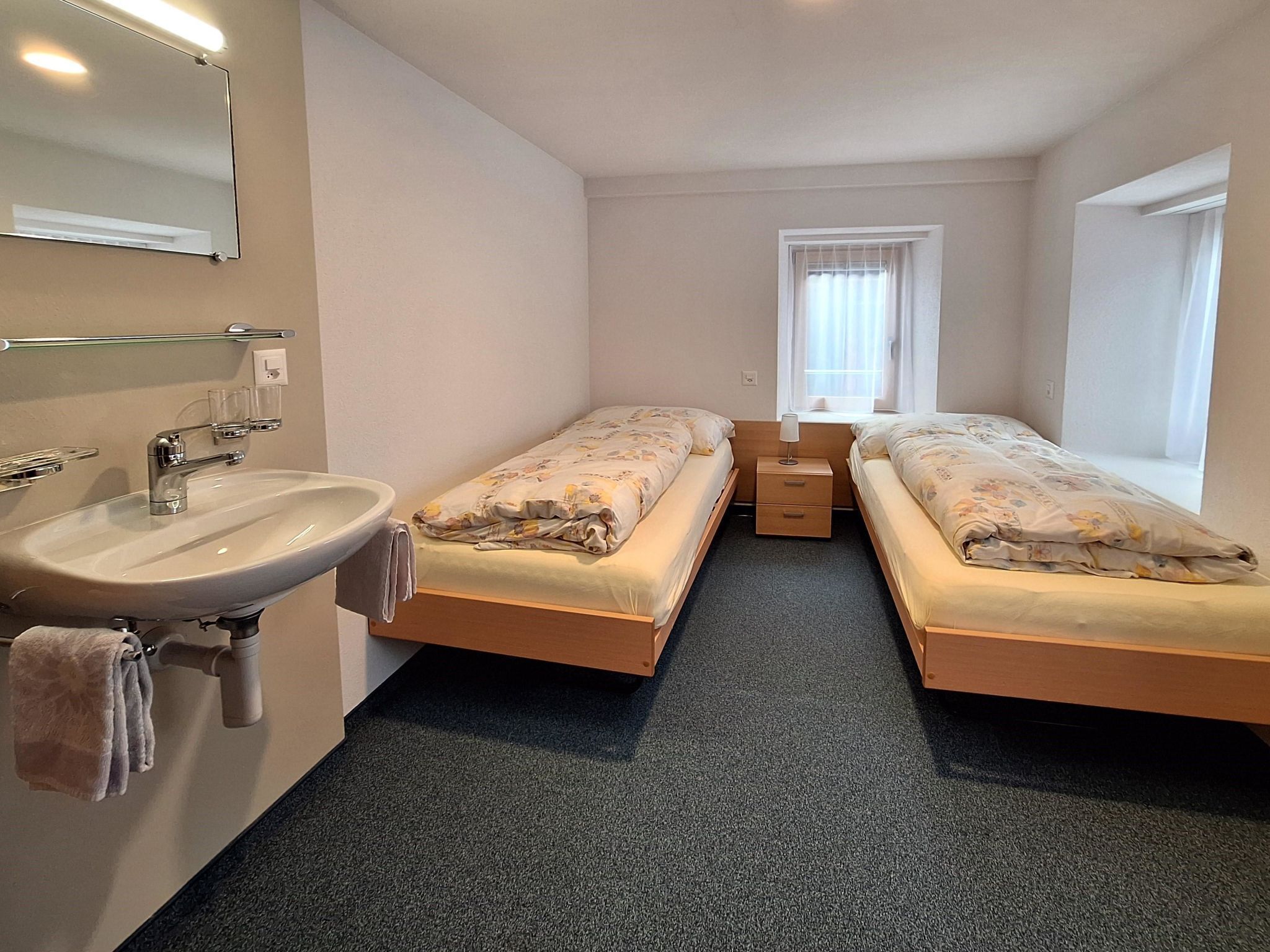 A hotel room with two single beds, a bathroom with a sink and mirror, and a window with curtains.