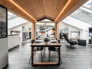 A modern dining area with a wooden table, black chairs, and a view of a mountain landscape through large windows. - Kusi's Ranch Appartement/Fewo Dachwohnung by Interhome (Saas-Fee)