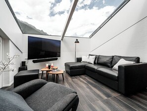 A modern living room with a sectional sofa, a flat-screen TV mounted on the wall, a small table with candles, and a floor lamp. - Kusi's Ranch Appartement/Fewo Dachwohnung by Interhome (Saas-Fee)