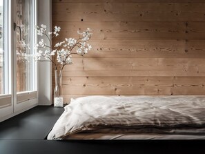 A bedroom with a wooden wall, a window with white curtains, and a bed with a white sheet. - Kusi's Ranch Studio Studio Nr. 11 Täschhorn by Interhome (Saas-Fee)