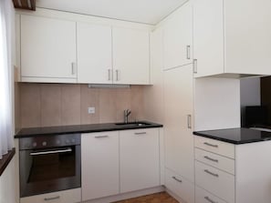 A compact kitchen with white cabinets, a black countertop, and stainless steel appliances including a stove and oven. - Floralpina Appartement/Fewo Wohnung Nr. 507 by Interhome (Saas-Fee)