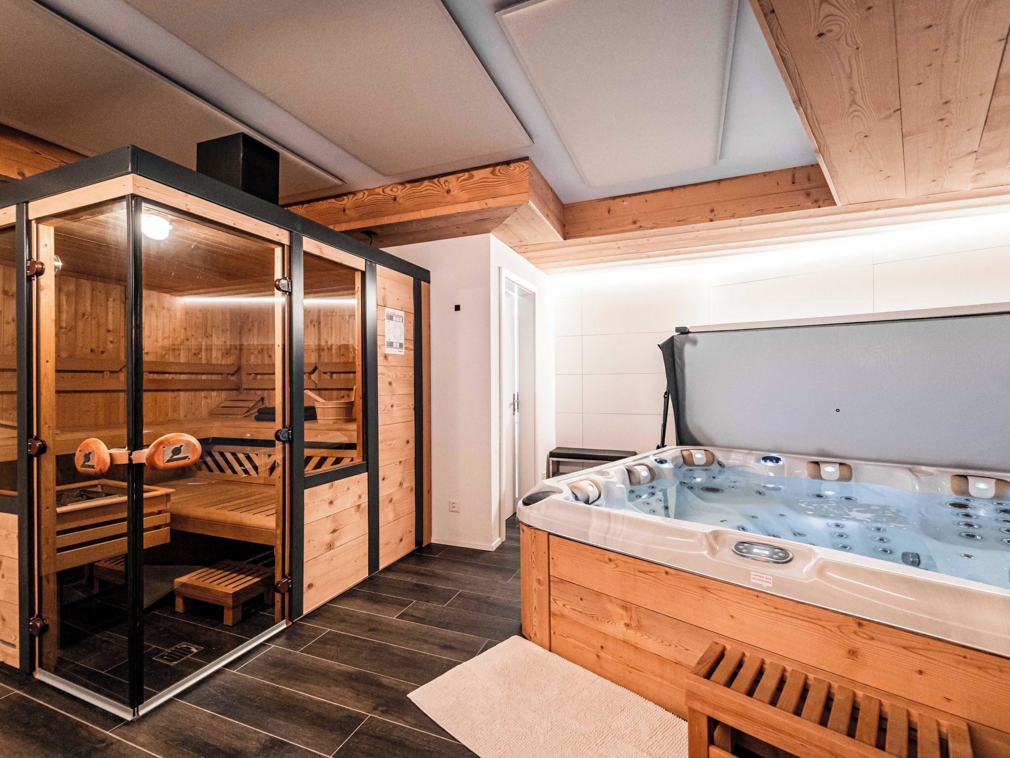 Een sauna met een houten bank en een glazen deur, een hottub met houten rand en een betegelde vloer.
