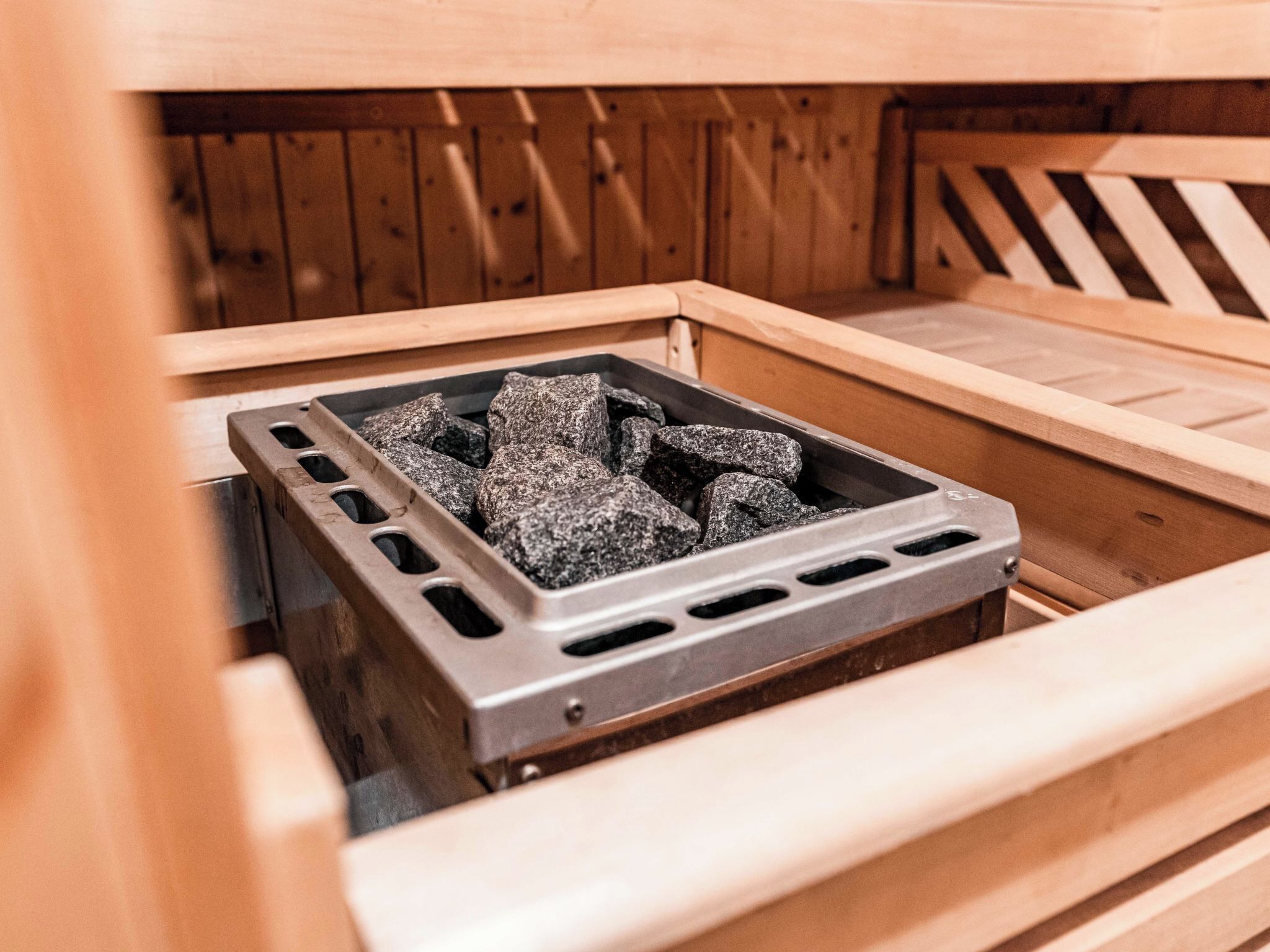 Un sauna doté d’une grille métallique remplie de pierres, de bancs en bois et d’un mur en bois.