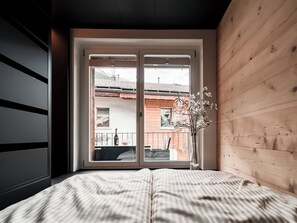Een slaapkamer met een groot raam, een bed met gestreepte beddengoed en een houten wand.