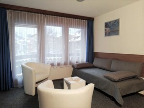 Ein Hotelzimmer mit einer Couch, zwei Sesseln, einem kleinen Tisch und einem Fenster mit Vorhängen.