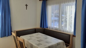 A room with a table and a bench, a cross on the wall, and a window with curtains. - Floralpina Appartement/Fewo Wohnung Nr. 506 by Interhome (Saas-Fee)
