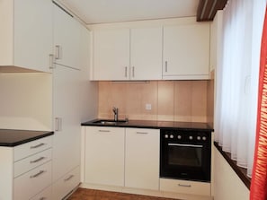 A compact kitchen with white cabinets, a black countertop, and a built-in oven. - Floralpina Appartement/Fewo Wohnung Nr. 505 by Interhome (Saas-Fee)