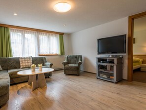 Un salon comprenant un canapé, un fauteuil, une table basse et un téléviseur posé sur un meuble.