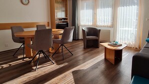 Ein modernes Wohnzimmer mit Essbereich, Holzböden und großen Fenstern mit leichten Vorhängen.