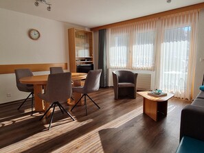 Ein modernes Wohnzimmer mit Essbereich, Holzböden und großen Fenstern mit leichten Vorhängen.