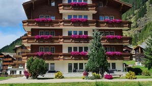 Ein mehrstöckiges Hotel mit Balkonen, die mit Blumen geschmückt sind, vor einer Berglandschaft.