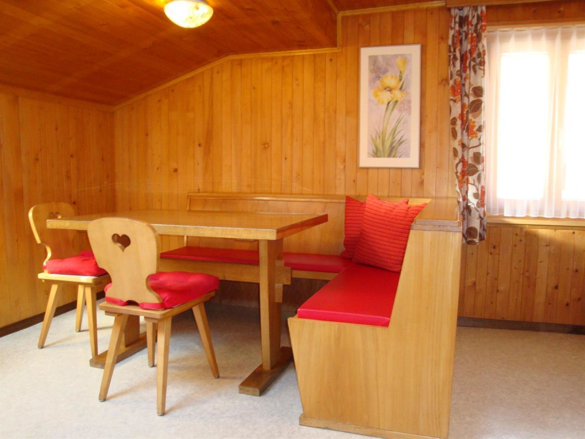 Ein Holzinnenraum mit Holztisch und -bank, roten Kissen und einem gerahmten Bild an der Wand.