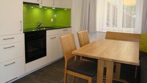 Una cocina moderna con armarios blancos, un salpicadero verde, una estufa negra y una mesa de comedor de madera con sillas.