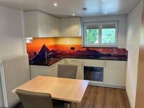 A compact kitchen with white cabinets, a black countertop, and a mountain-themed backsplash. - Morgenrot Appartement/Fewo 4-Bettwohnung Nr. 2 by Interhome (Saas-Grund)
