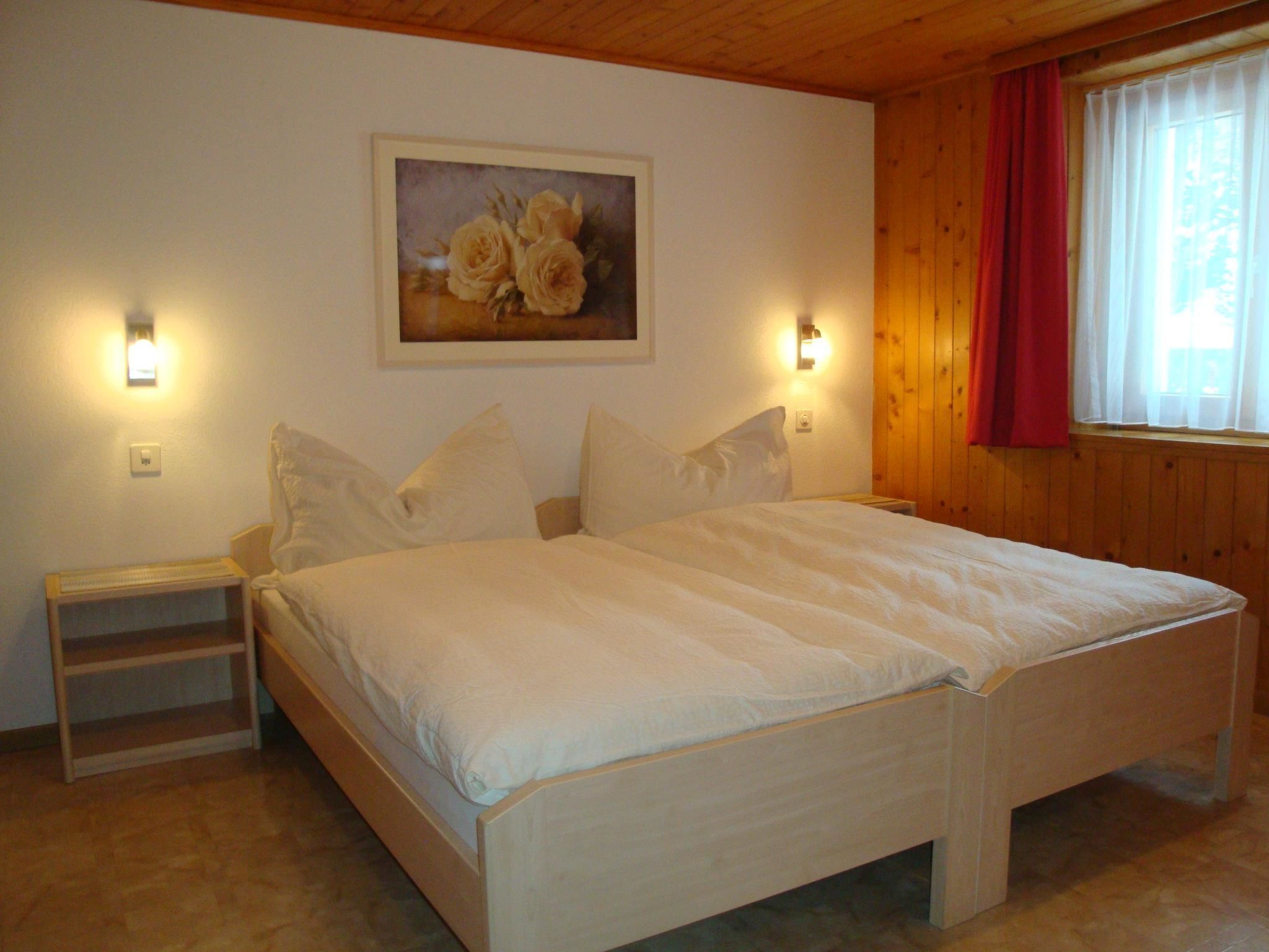 Een slaapkamer met een groot bed, twee nachtkastjes, een wandlamp, een schilderij en een raam met gordijnen.