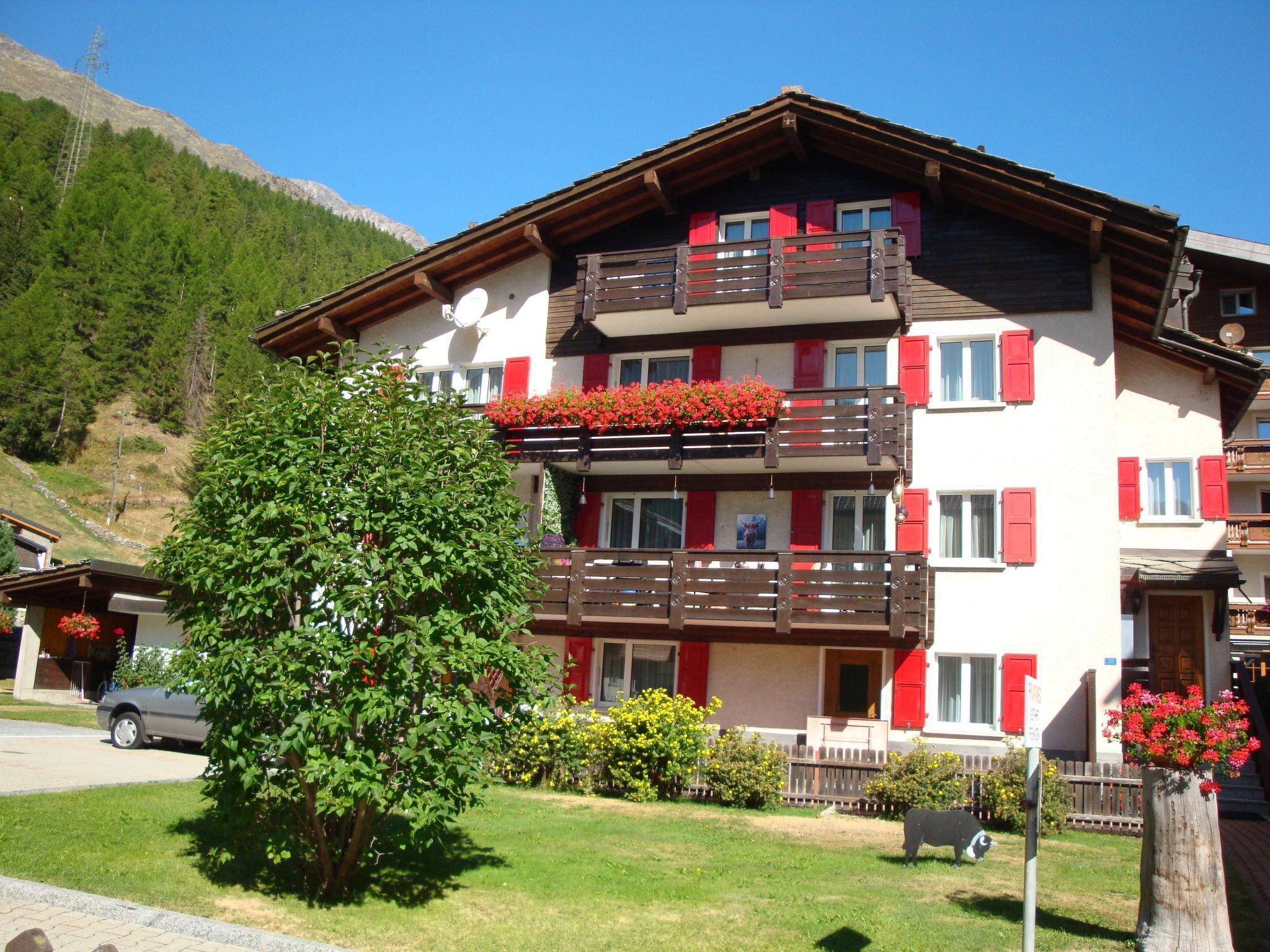 Un immeuble à plusieurs étages doté de balcons, avec un arbre au premier plan et une chaîne de montagnes en arrière-plan.