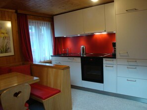 Una cocina compacta con armarios blancos, una estufa negra y una pared de acento roja.