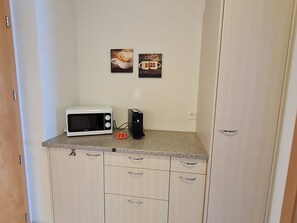 Eine Küchenzeile mit einer weißen Mikrowelle, einer Kaffeemaschine und zwei gerahmten Bildern an der Wand.
