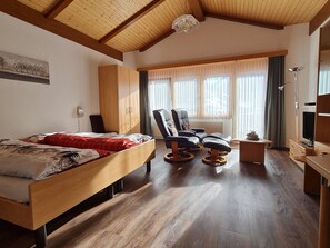 Een kamer met een houten bed, twee stoelen, een klein tafeltje, een televisie en een kledingkast.