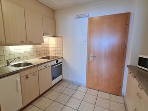 A compact kitchen with a dishwasher, oven, and a wooden door. - Orion Appartement/Fewo 2-Bettwohnung Nr. 50 by Interhome (Saas-Grund)