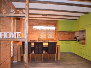 A dining area with a wooden table and chairs, a kitchen with green cabinets, and a 'HOME' sign on the wall. - Alpenperle Appartement/Fewo 5-Bettwohnung by Interhome (Saas-Almagell)
