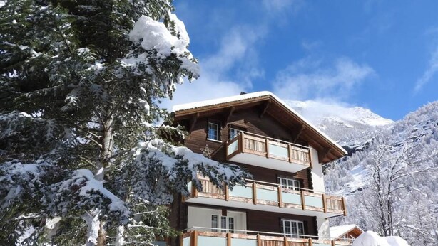 Una chalet a più piani con balconi, circondata da alberi innevati e montagne.