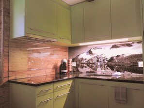 A kitchen with green cabinets, a countertop, and a wall-mounted coffee machine. - Alpenperle Appartement/Fewo 5-Bettwohnung by Interhome (Saas-Almagell)