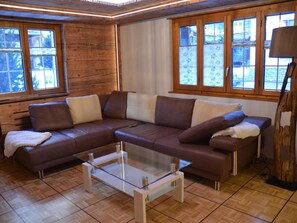 A modern living room with a leather sectional sofa, a glass coffee table, and large windows providing natural light. - Alpenperle Appartement/Fewo 5-Bettwohnung by Interhome (Saas-Almagell)