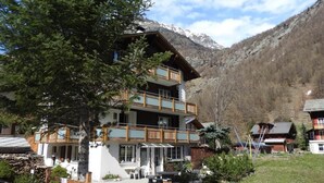 Un edificio a più piani con balconi, una zona salotto esterna coperta e montagne sullo sfondo.
