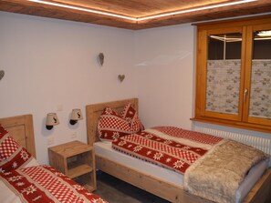 A bedroom with two beds, wooden headboards, a small bedside table, wall-mounted lamps, and a window with blinds. - Alpenperle Appartement/Fewo 5-Bettwohnung by Interhome (Saas-Almagell)