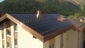 A building with a solar panel roof, a chimney, and a mountainous backdrop. - Azur Appartement/Fewo 2-Bettwohnung Nr. 3 by Interhome (Saas-Fee)