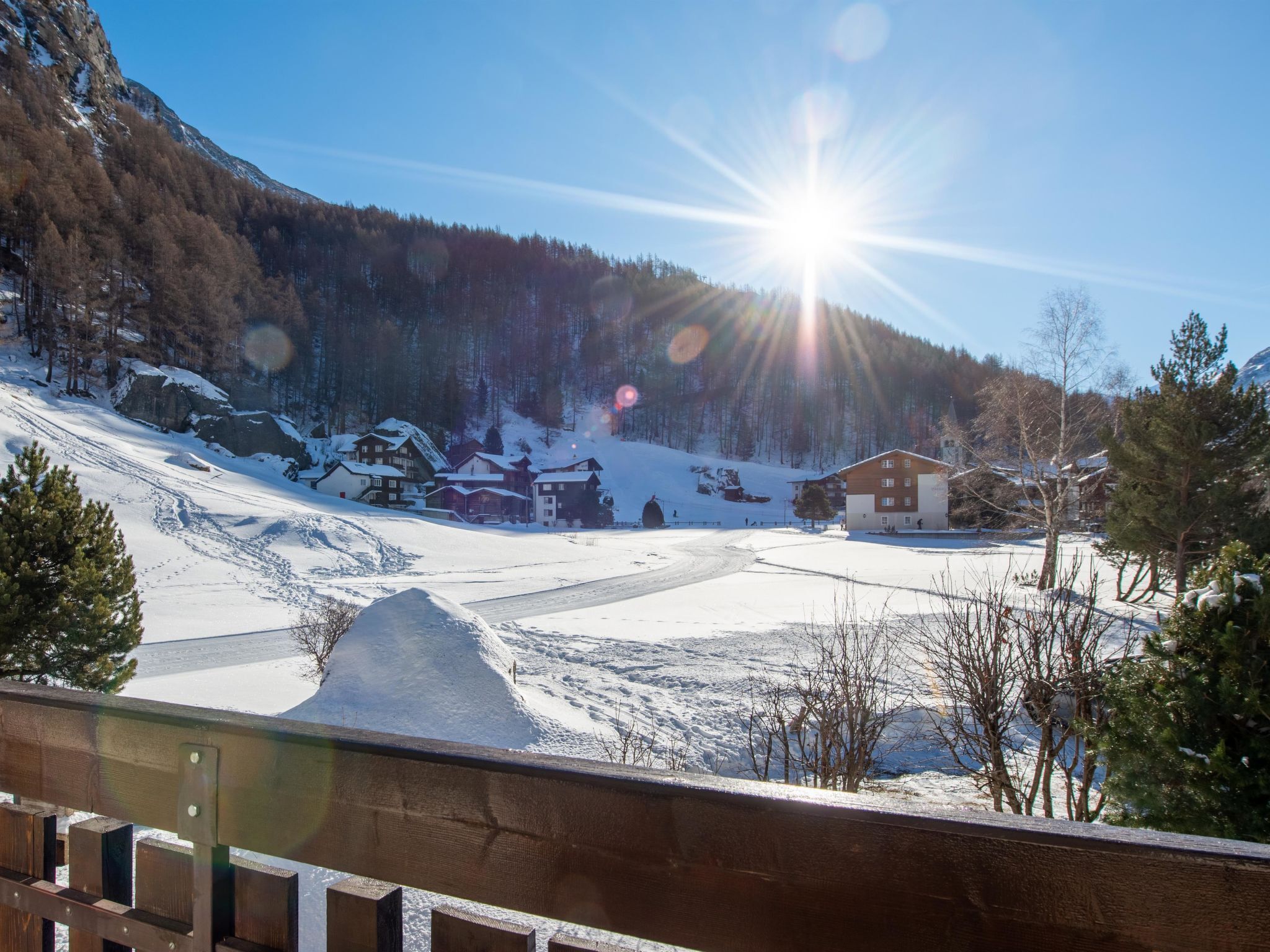 A snow-covered landscape with buildings, a wooden fence, and a clear sky.