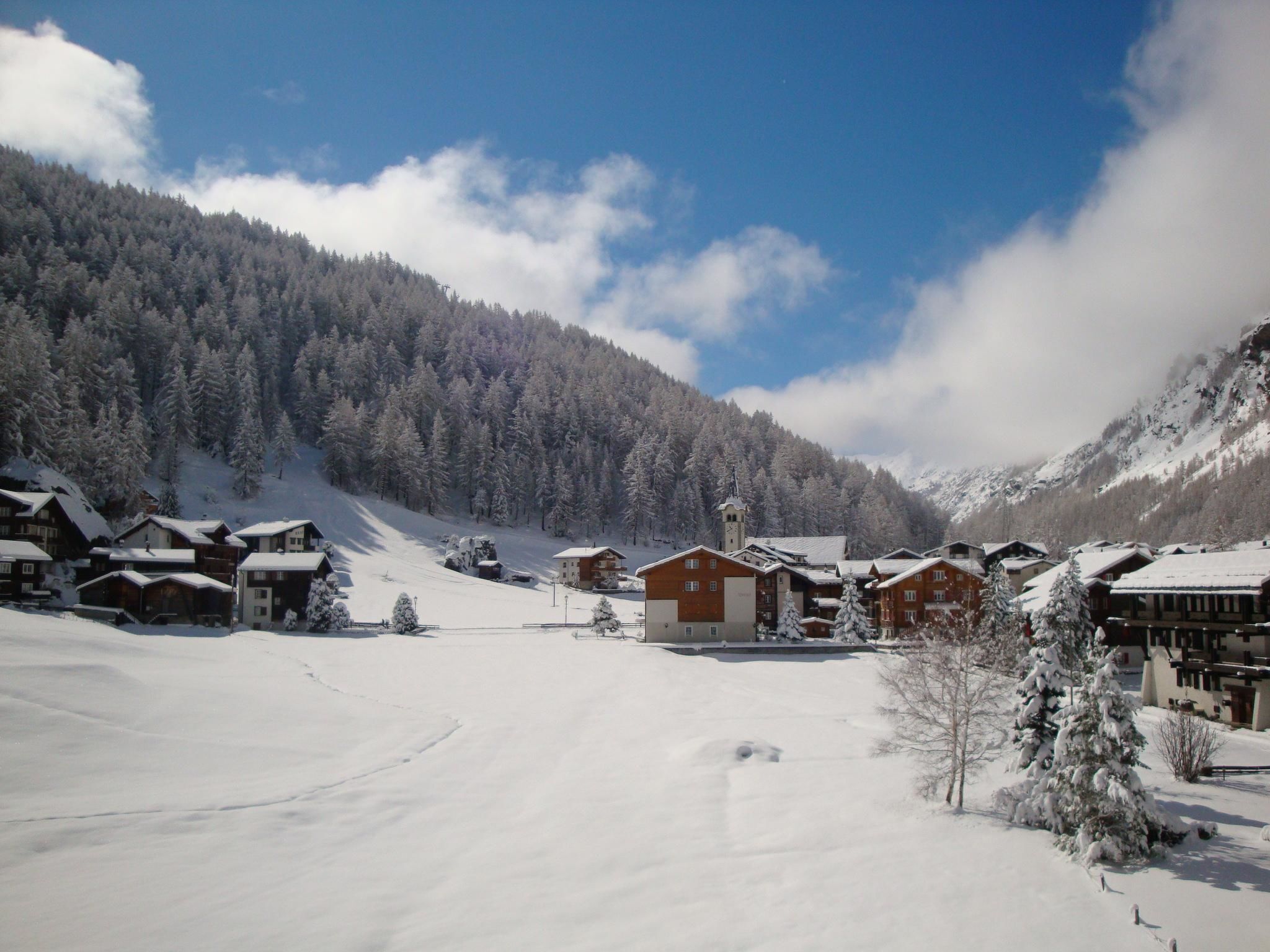 A snow-covered village with wooden buildings, a ski slope, and a mountain backdrop.