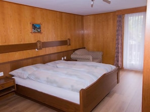 Une chambre à coucher aux murs lambrissés, avec un lit, une table de chevet et une fenêtre avec des rideaux.