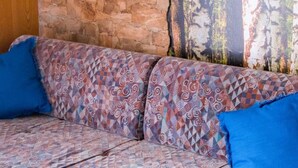 A sofa with a patterned fabric and two blue cushions against a stone wall and a forest mural. - Monte Rosa Appartement/Fewo Appartement Weissmies by Interhome (Saas-Grund)