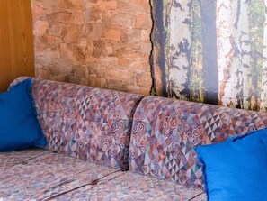 Un sofá con tela estampada y dos cojines azules, frente a una pared de piedra y un mural con un bosque.