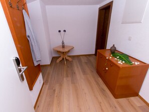 Ein kleiner, sauberer Raum mit Holzboden, einem Tisch mit einer Vase und einem Schminktisch mit Dekoration.