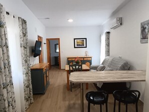 Ein gemütlicher Wohnbereich mit Essplatz, einer Couch, einem Fernseher und einem Bild an der Wand.