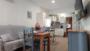 A modern living room with a sofa, dining table, chairs, and a TV mounted on the wall. - Villa Franca House | Rural Holiday Home with 1 Bedroom, Shared Pool and parking (Orgiva)