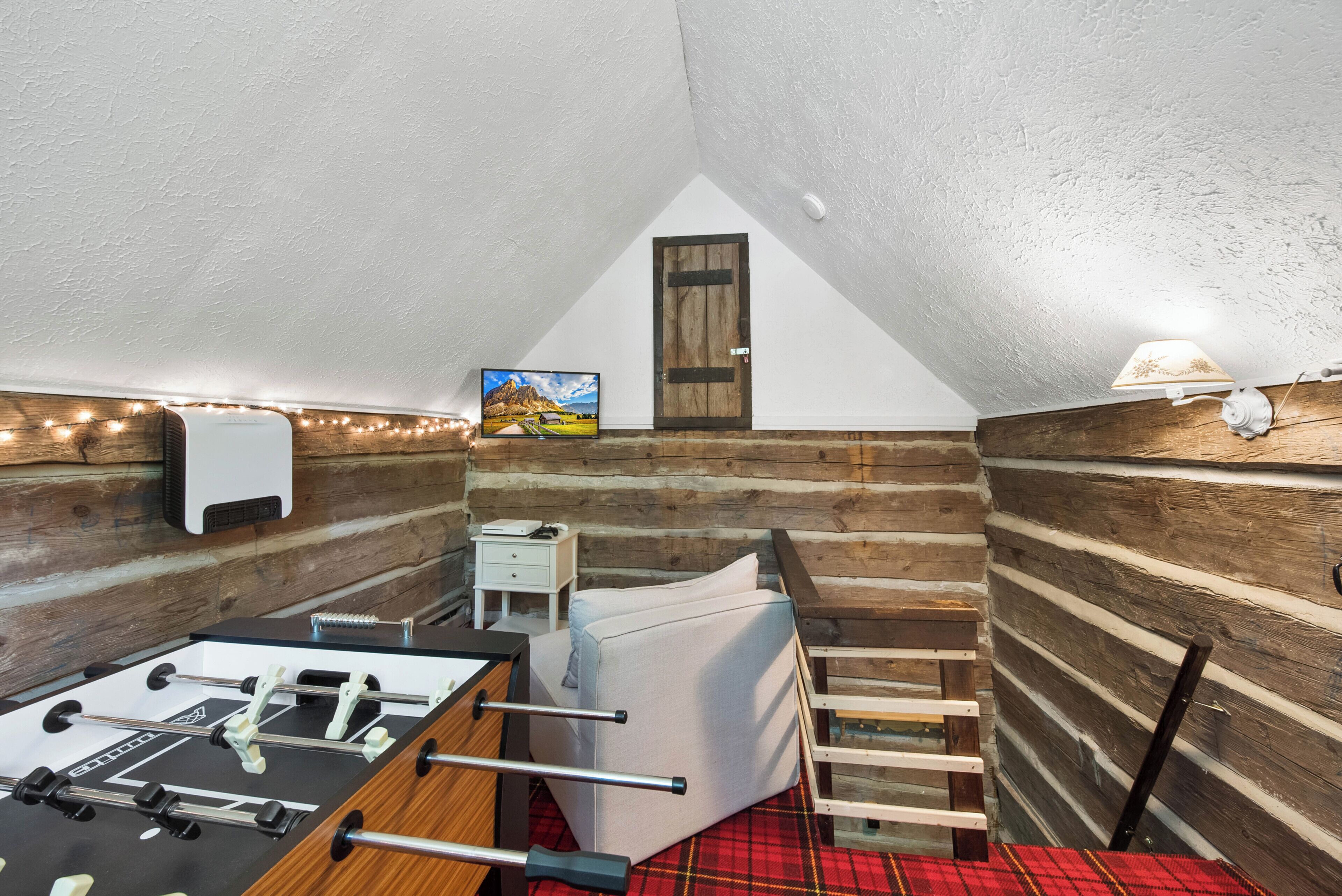 A cozy attic room with a foosball table, a bed, a small desk, and a painting on the wall.