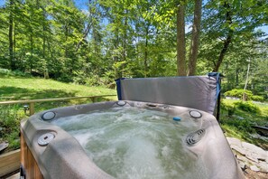 Un bain à remous situé dans un espace boisé, doté d’une terrasse en bois et offrant une vue sur la végétation environnante.