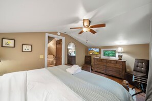 Une chambre à coucher comprenant un lit, un ventilateur de plafond, une commode, une chaise et un téléviseur.
