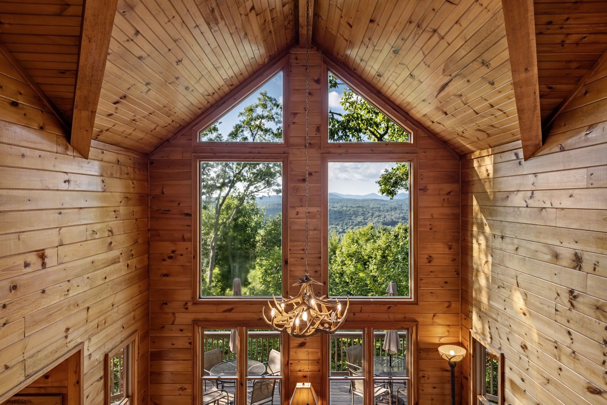 A wooden interior with a high ceiling, large windows, and a chandelier.