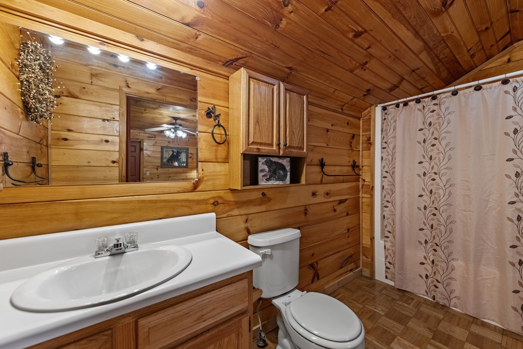 A wooden cabin bathroom with a white sink, toilet, and shower curtain.
