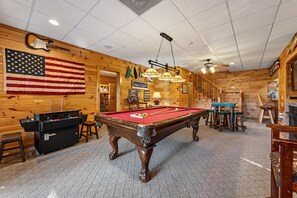 A pool table in a room with wooden walls, a flag, and a ceiling fan. - A Touch of Bearadise - Mountain View | Pet Friendly | Close to Town! | Game Room | Firepit | (Morganton)