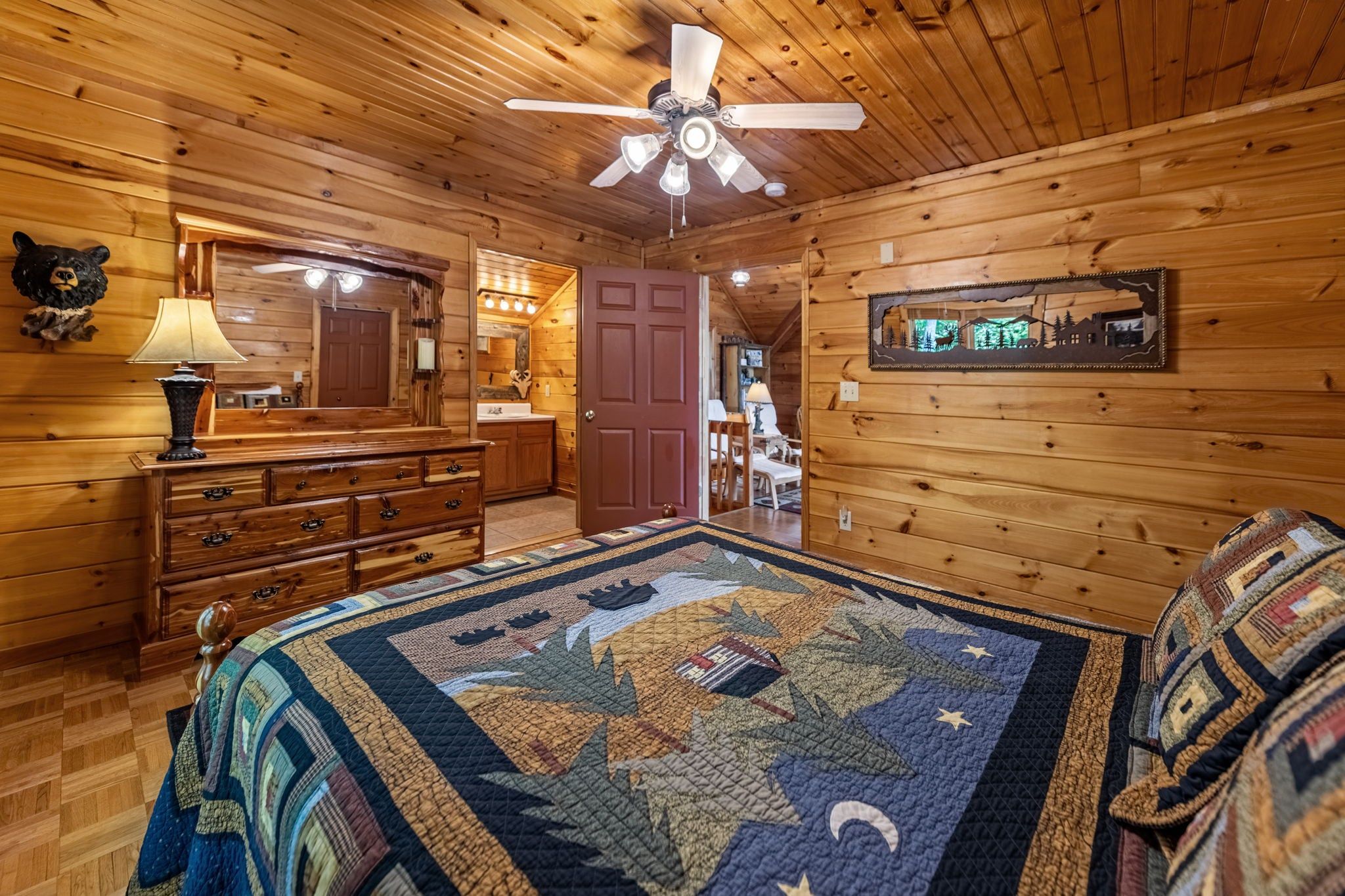 A wooden cabin interior with a bed, dresser, and a ceiling fan.