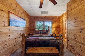 Een interieur van een blokhut met een bed, een raam en een plafondventilator.