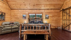 A wooden cabin interior with a bed, a leather sofa, and a bench. - Bear Claw Lodge - Pet Friendly | Firepit | Outdoor Fireplace | Hot Tub (Cherry Log)