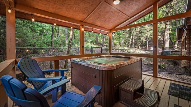 A hot tub with wooden deck seating, surrounded by large windows offering forest views. - Bear Claw Lodge - Pet Friendly | Firepit | Outdoor Fireplace | Hot Tub (Cherry Log)