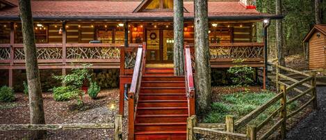 A cabin with a staircase leading to a wooden deck, surrounded by trees.